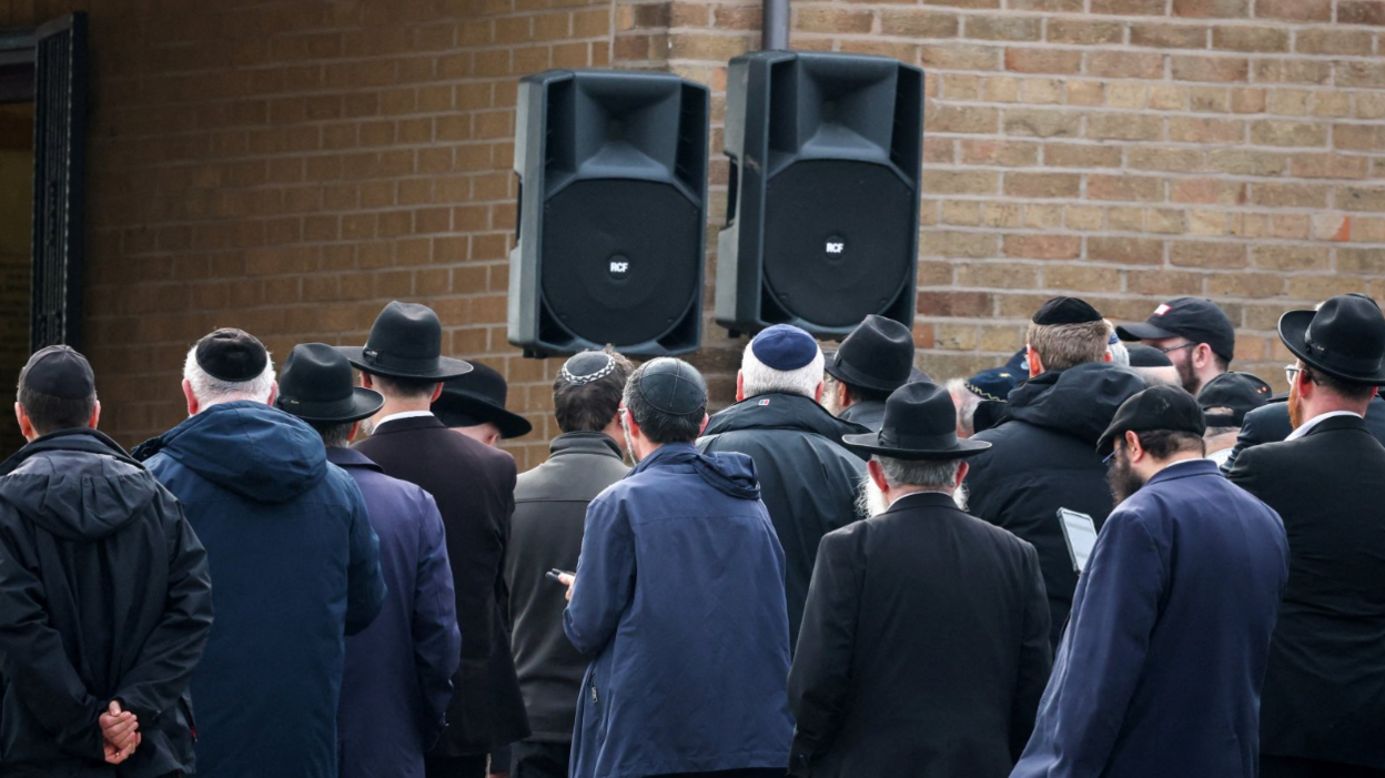 Traditionally dressed mourners at the service, pictured outside with two large speakers relaying the ceremony