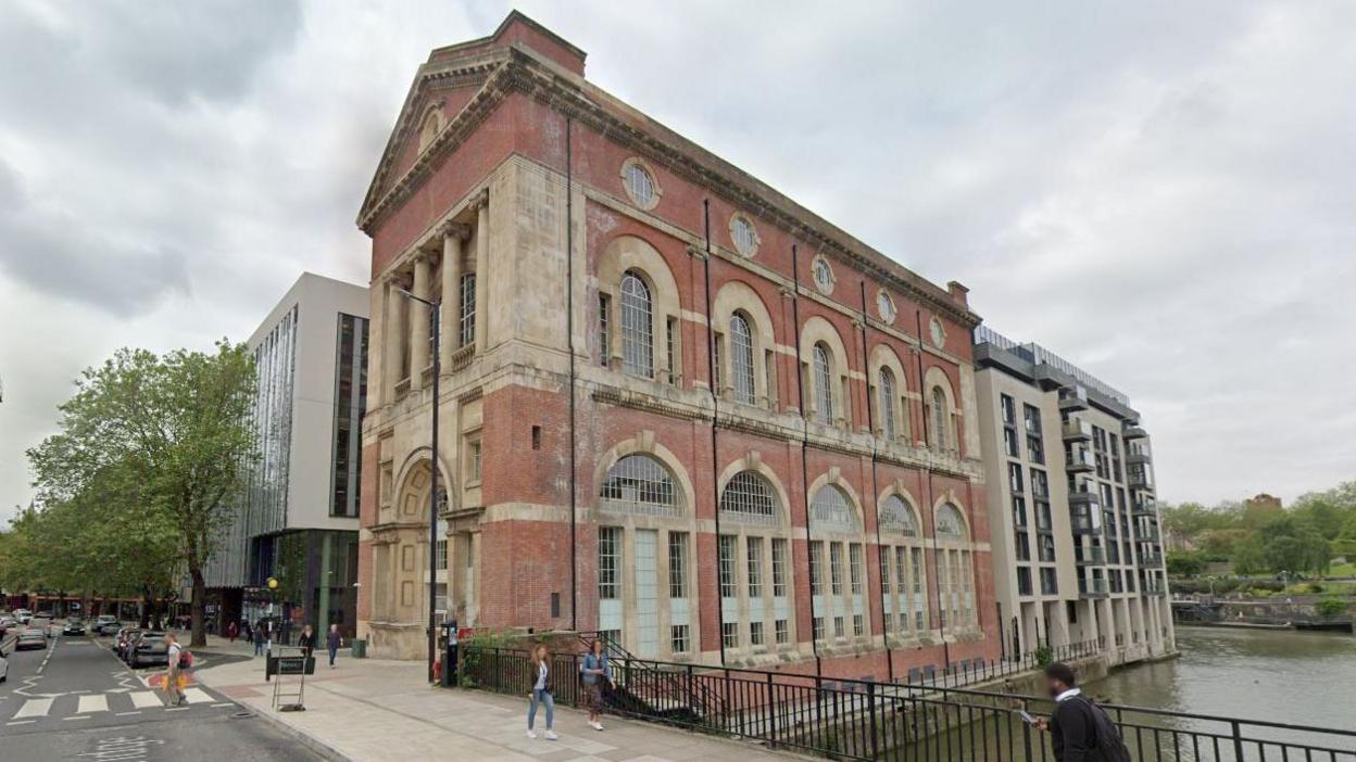 The old electricity generating station for Bristol Tramways. It is a large red and sandstone coloured building with arched windows and pillars at the front, above a large arched entrance. The building is situated just off St Philip's Bridge and you can see the river flowing just beside it.