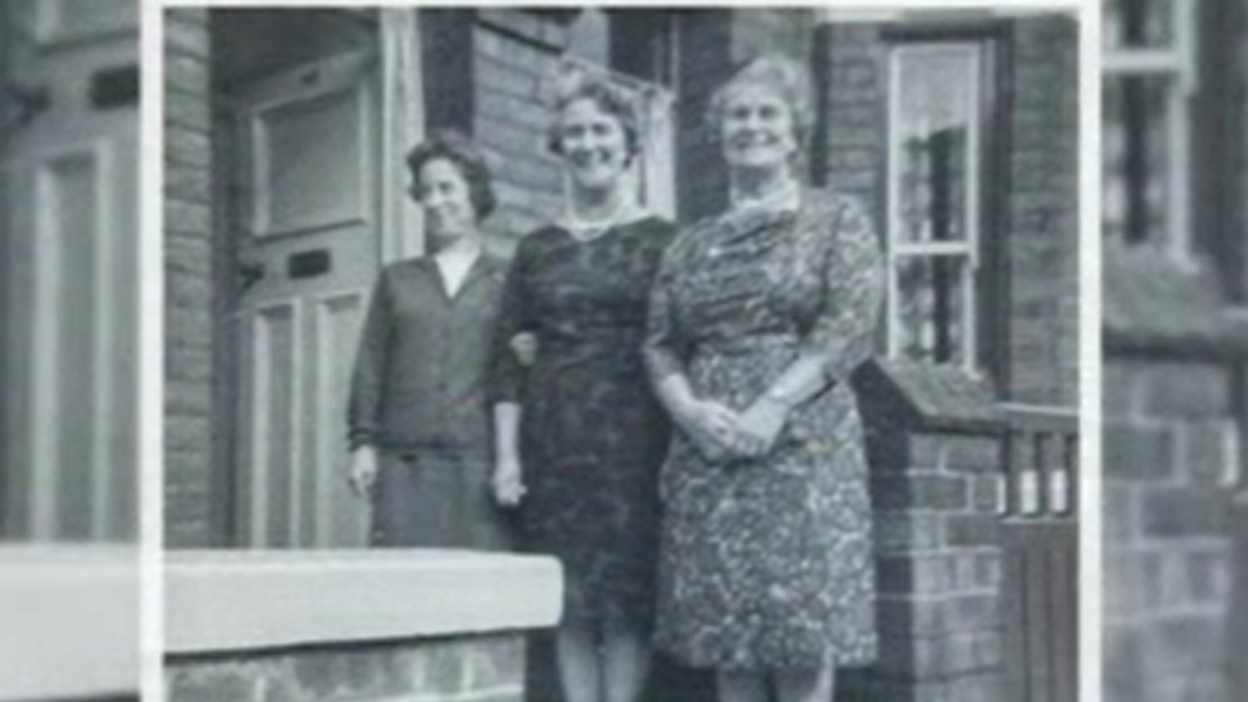 Black-and-white photo of Andrew Hay's grandma Elsie Hay, on the steps of her former home in Siward Street, York. Elsie has her hands clasped in front of her, is smiling at the camera and is wearing a floral dress.