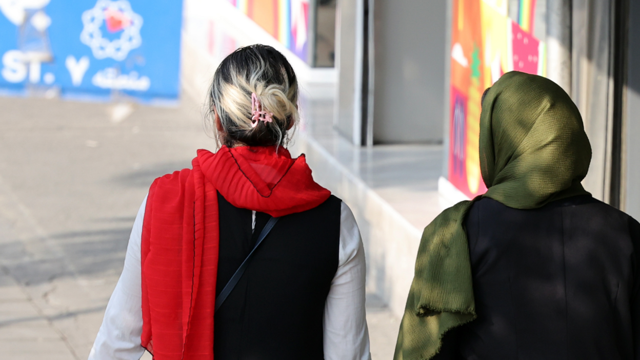 An Iranian woman (l) without a mandatory headscarf, or hijab, walks in a street in Tehran, Iran next to a woman wearing a headscarf on15 September 2024