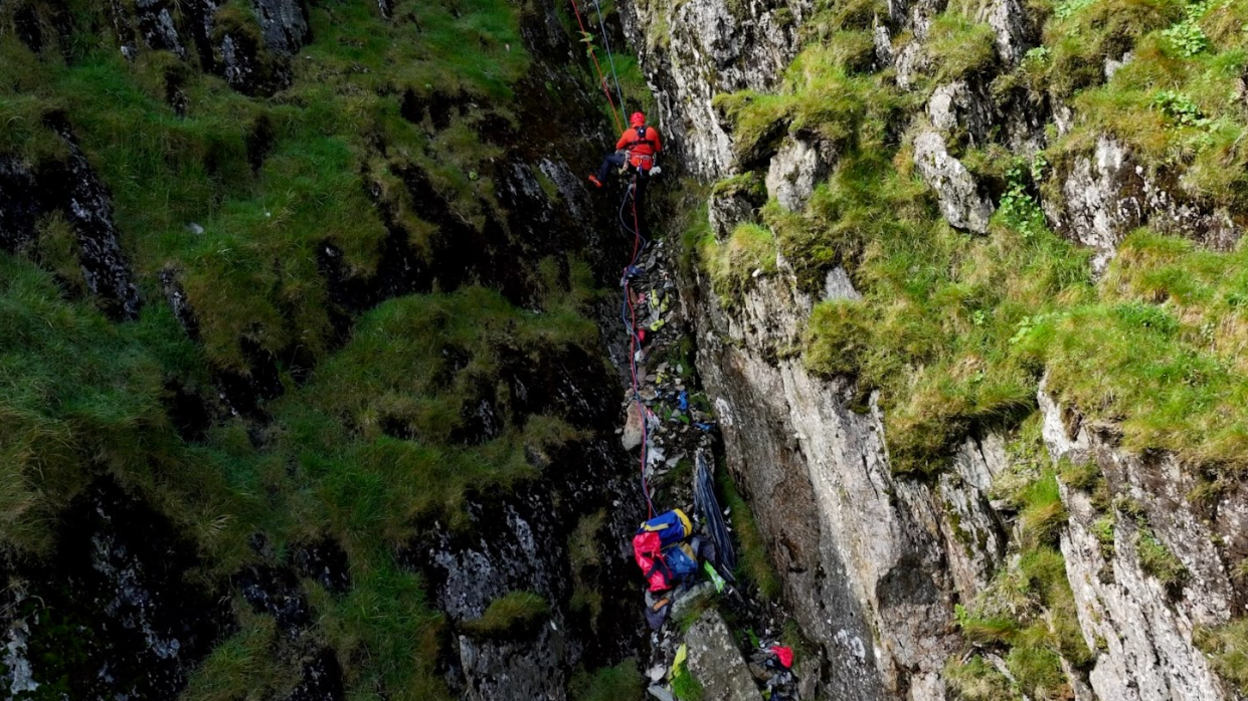 An aerial view of a mountain side with a number of abseilers on ropes scaling it.