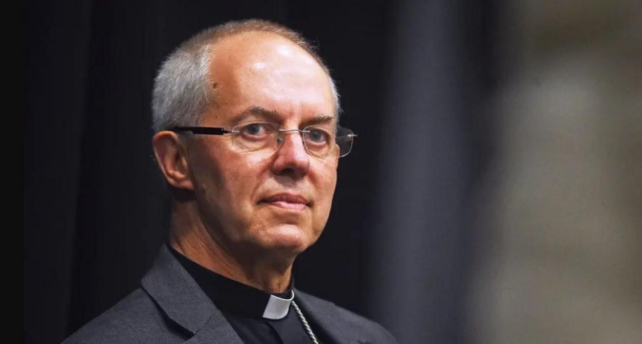 A head-and-shoulders picture of Justin Welby, who is wearing a reverend's collar, a dark grey jacket and glasses, He is looking directly at the camera. 