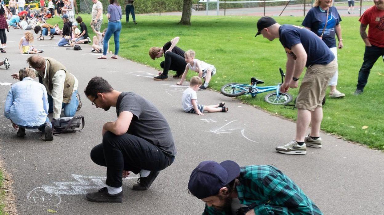 A number of people drawing lighting bolts on a pavement in a park 