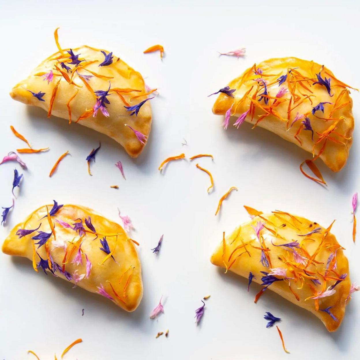 Pastries laid out on a white surface and garnished with blue, pink and orange leaves.