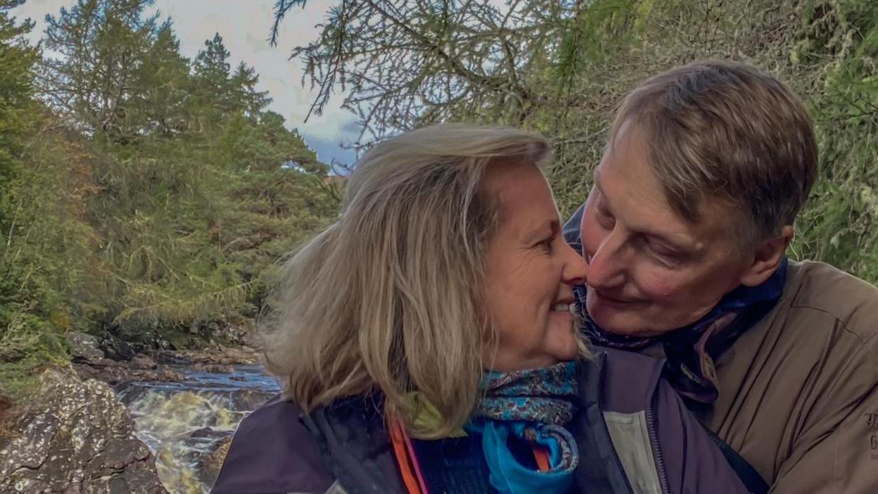 Prof Crellin with his wife about to share a kiss stood in front of a water fall 