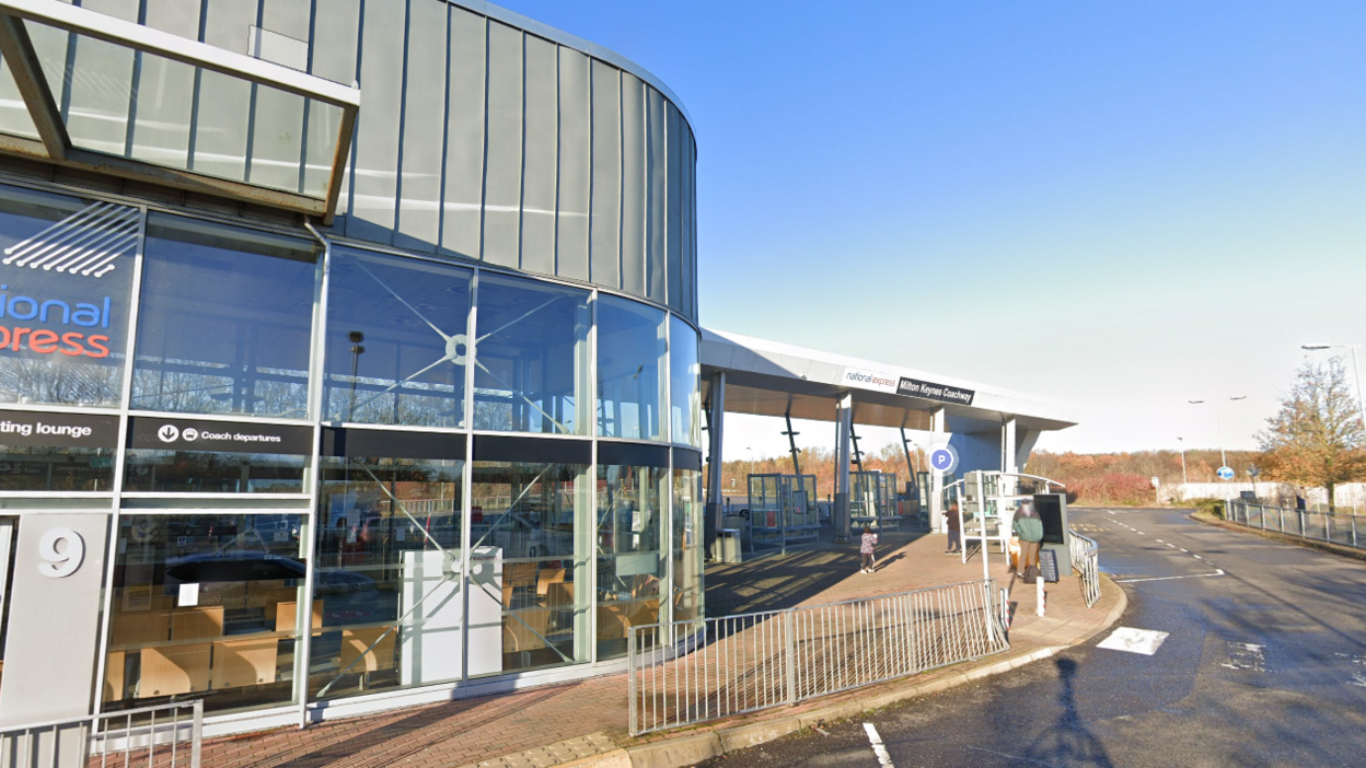 Milton Keynes Coachway: a glass-fronted building with a roadway in front of it and one person waiting for a coach