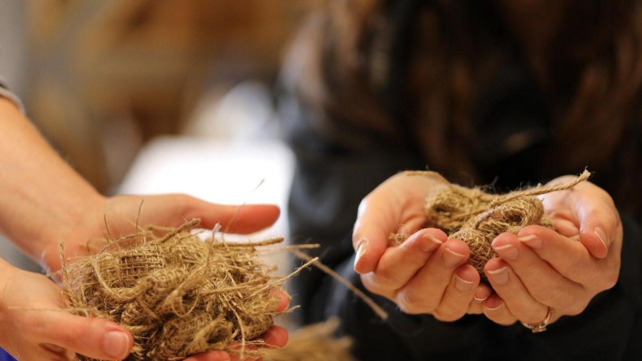 Close-up shot of two people's outstretched hands holding brown-coloured hessian seed bags 