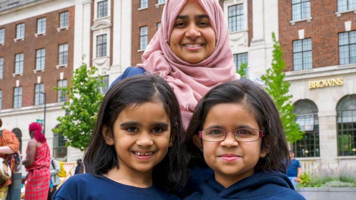 Lubna Siddiqui smiling for a picture with her two daughters Sofia and Fatima outside.
