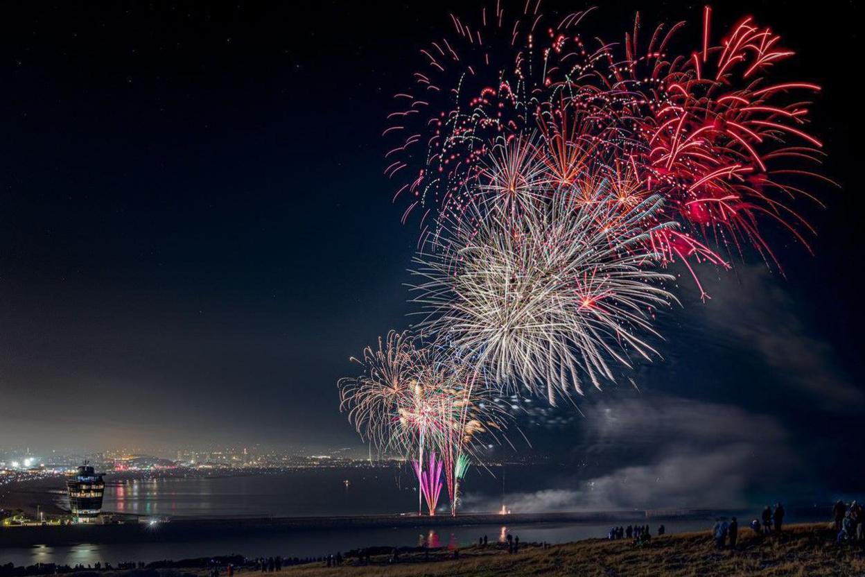 Red, white, gold and pink fireworks exploding over the harbour. In the background are the lights of Aberdeen.