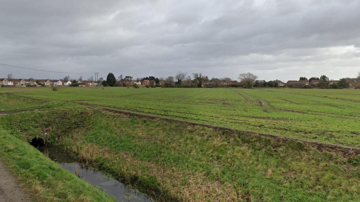 A green field with some houses on the edges.