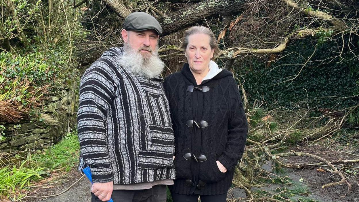 A bearded man with a black and white top and a cap and a woman with a black knitted top.