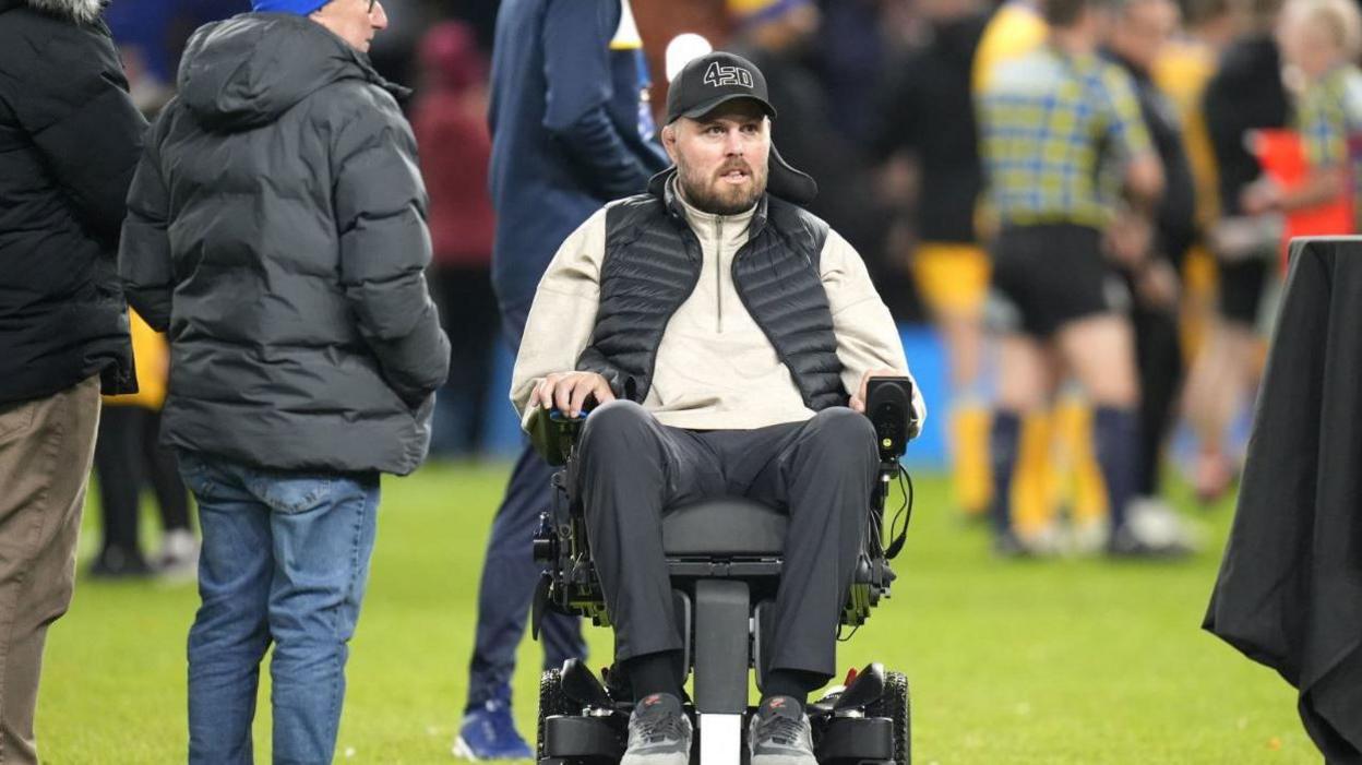 Ed Slater in a wheelchair watching a rugby game go on 