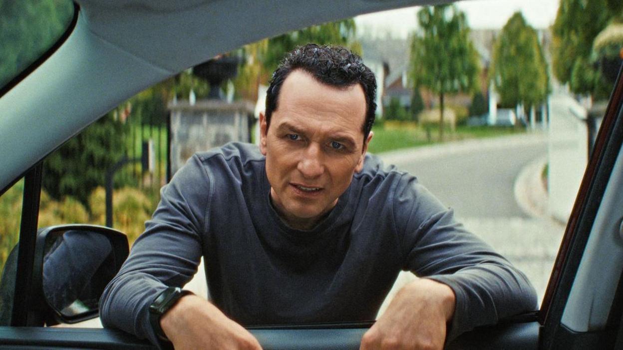 Matthew Rhys as Nile Jarvis in The Beast In Me peers through car window with a grimace