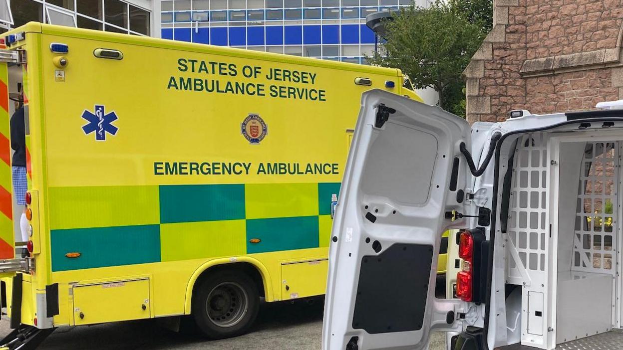 A States of Jersey Ambulance parked up with the doors open at the back. Nearer to the camera is the back of a police van which also has the doors open. 