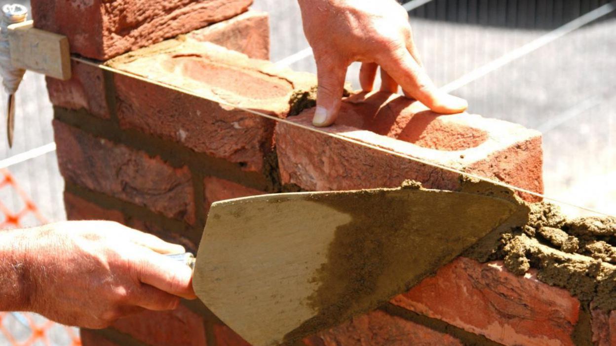 A man builds a wall using a trowel and a string level line.