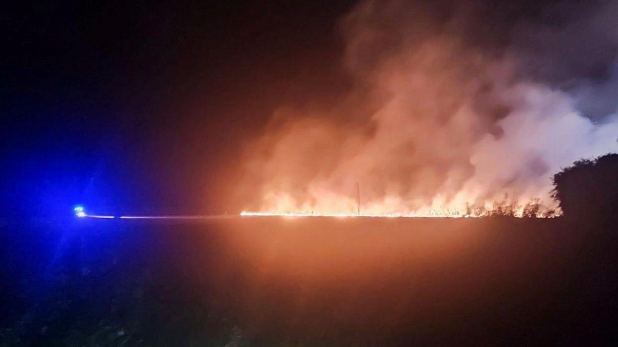 A blue light from an emergency vehicle near a fire in a field at night.