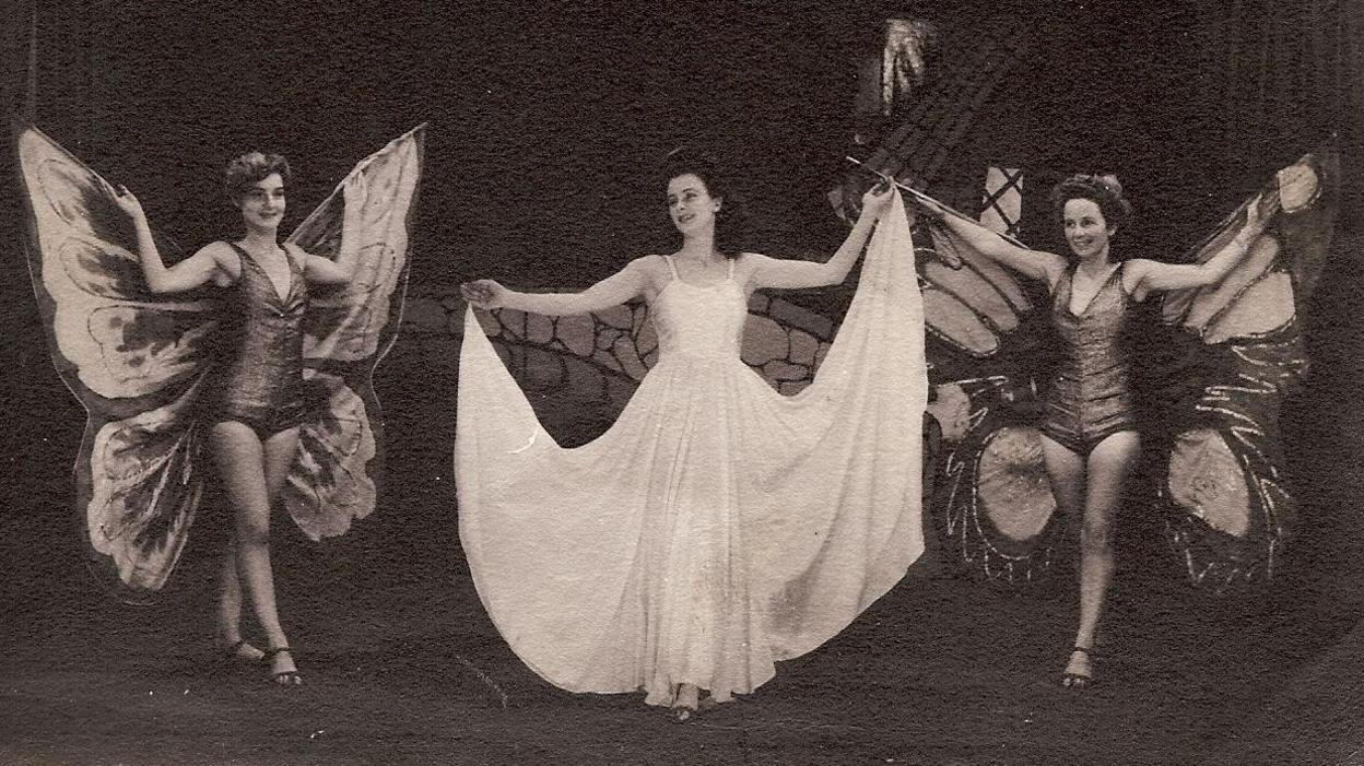 Women on stage with two dressed with butterfly wings and a woman in a white dress