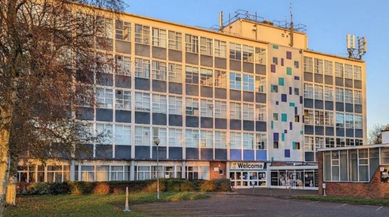 A five-storey building with many windows and a welcome sign outside on the ground floor.