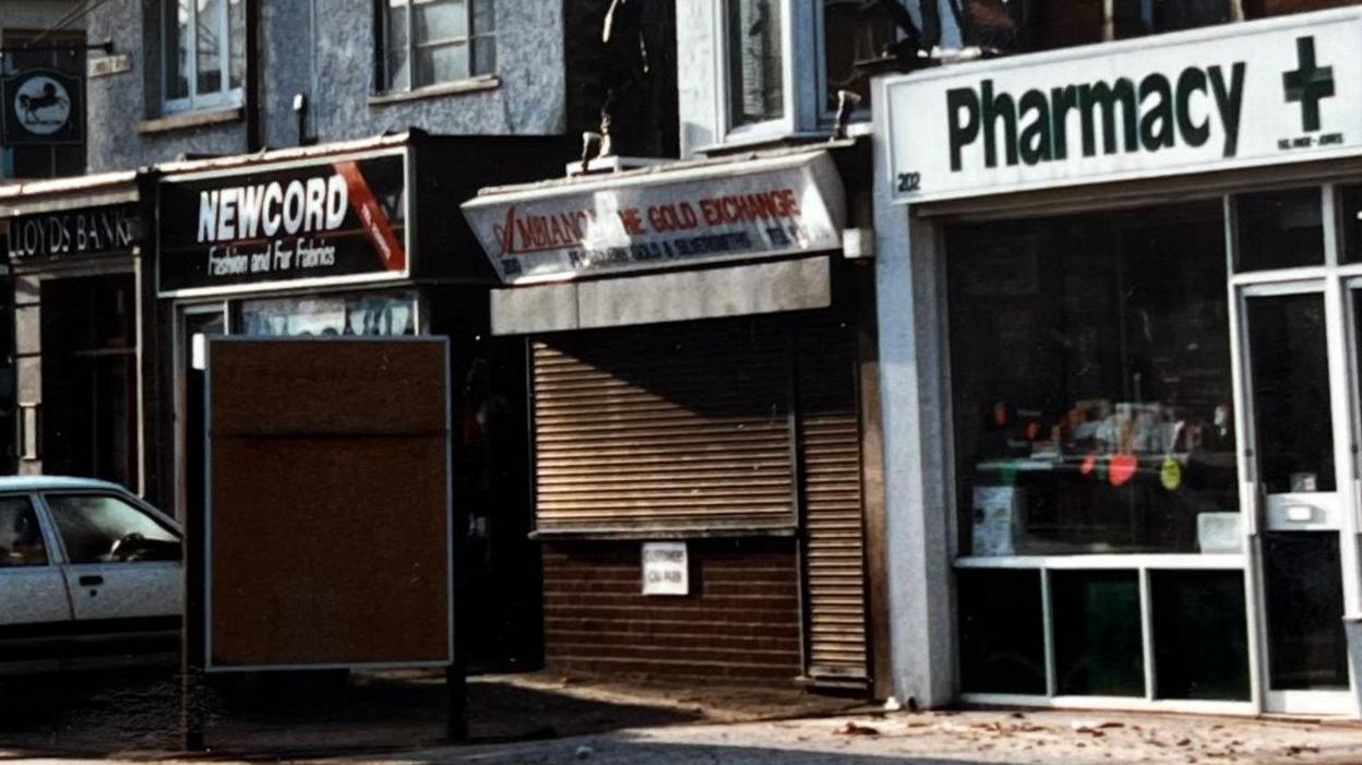 Archive picture of jewellery shop with shutters down, in between a pharmacy and fabric shop on Shirley Road