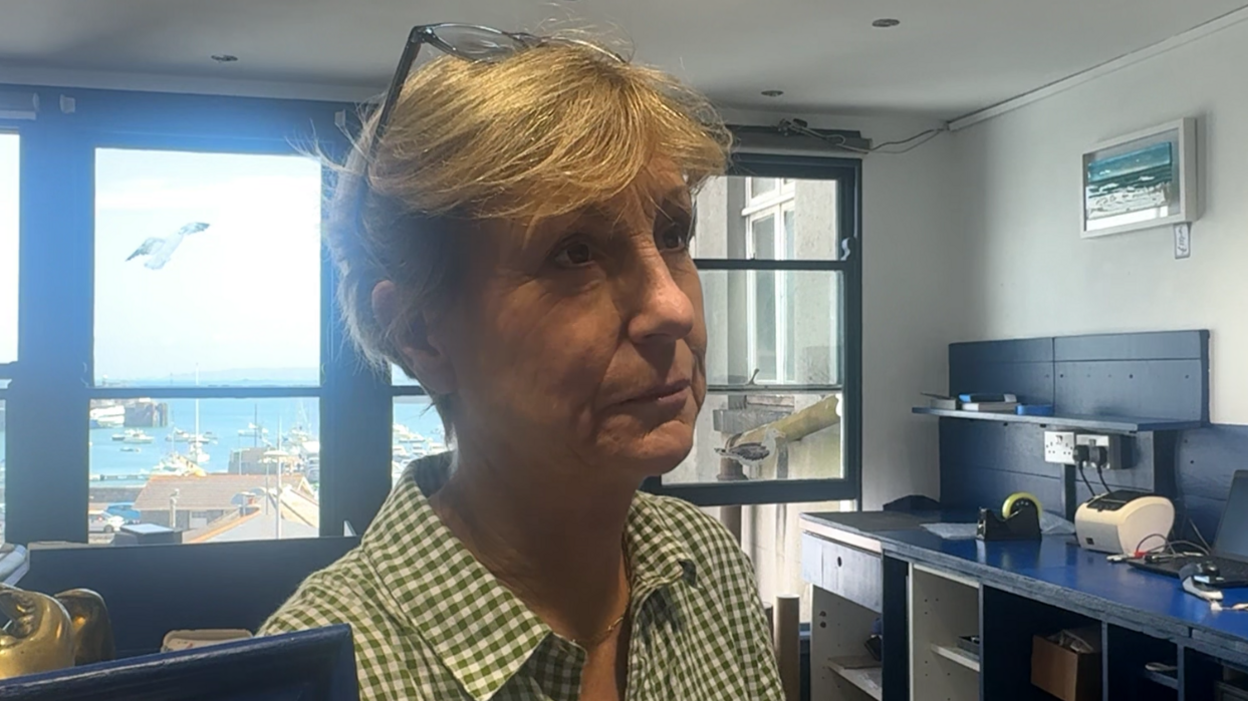A women with short blonde hair. She has a pair of glasses on her head. She is wearing a green and white gingham style shirt