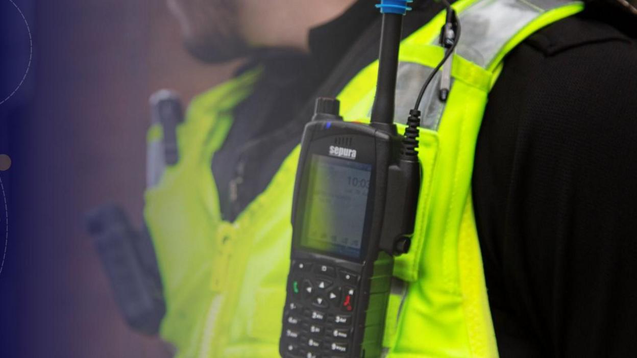 A police officer with his walkie talkie attached to his fluorescent jacket