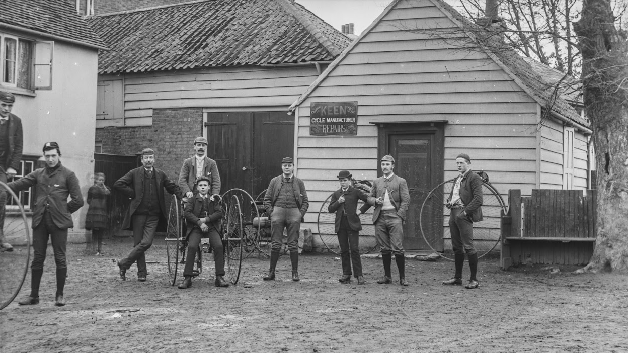 An historical photo of 10 people taken in Elmbridge. They are carrying large horse and carriage wheels, wearing boots and with hats.