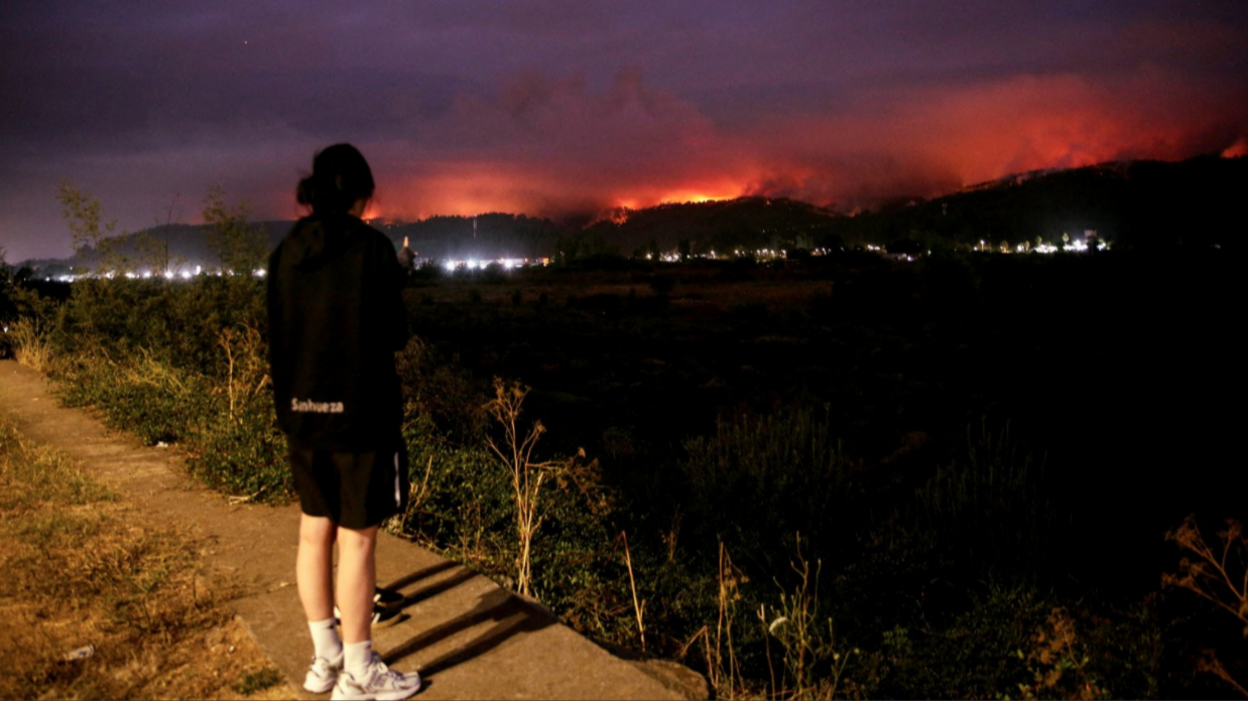 People watch smoke and fire rise as wildfire burns in Concepcion, Chile, in the aftermath of a forest fire.