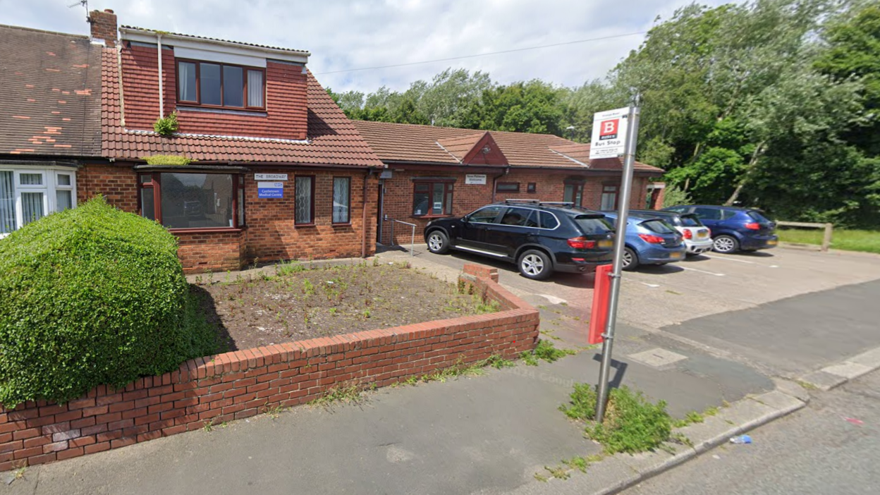 Castletown Medical Centre is a two-storey red brick building. There is blue and white sign at the front of the building with the NHS logo on it. 