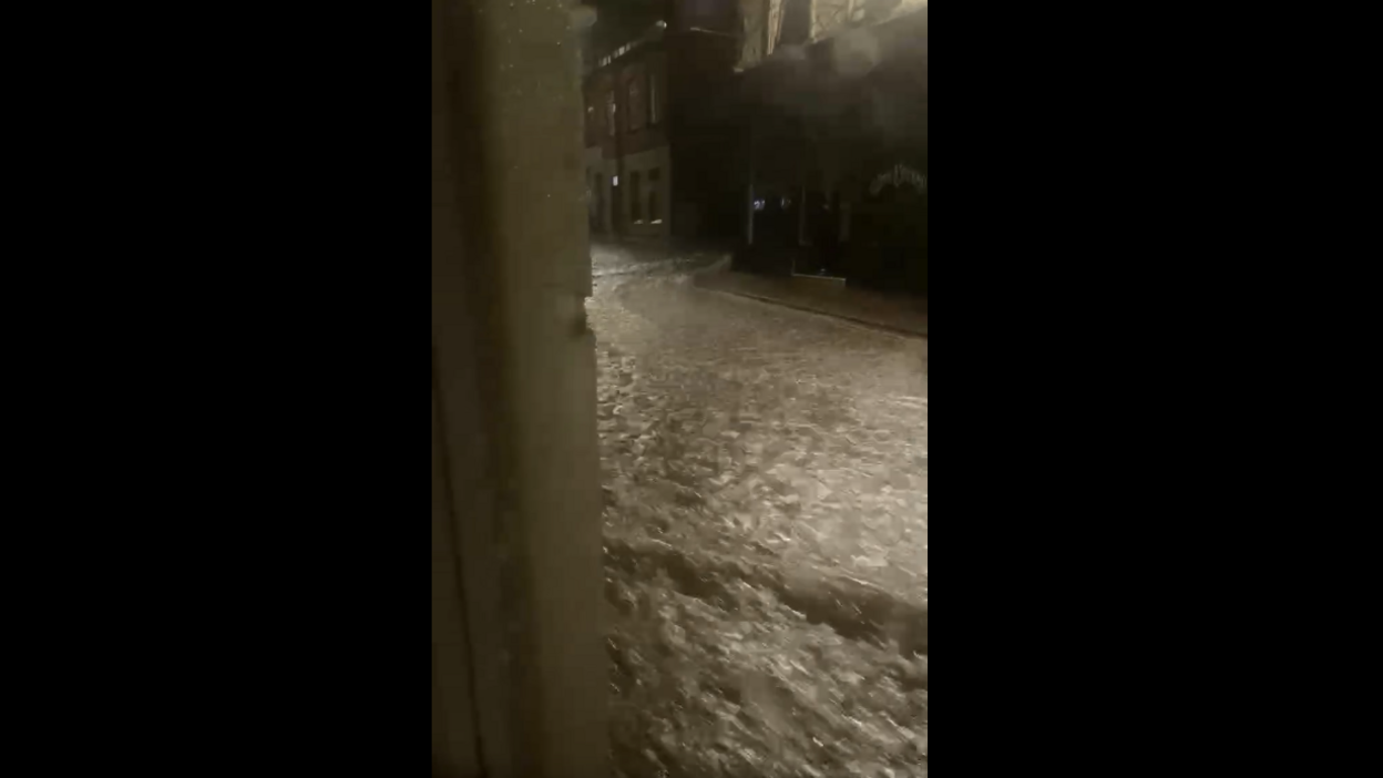 Water flows through a high street at night.