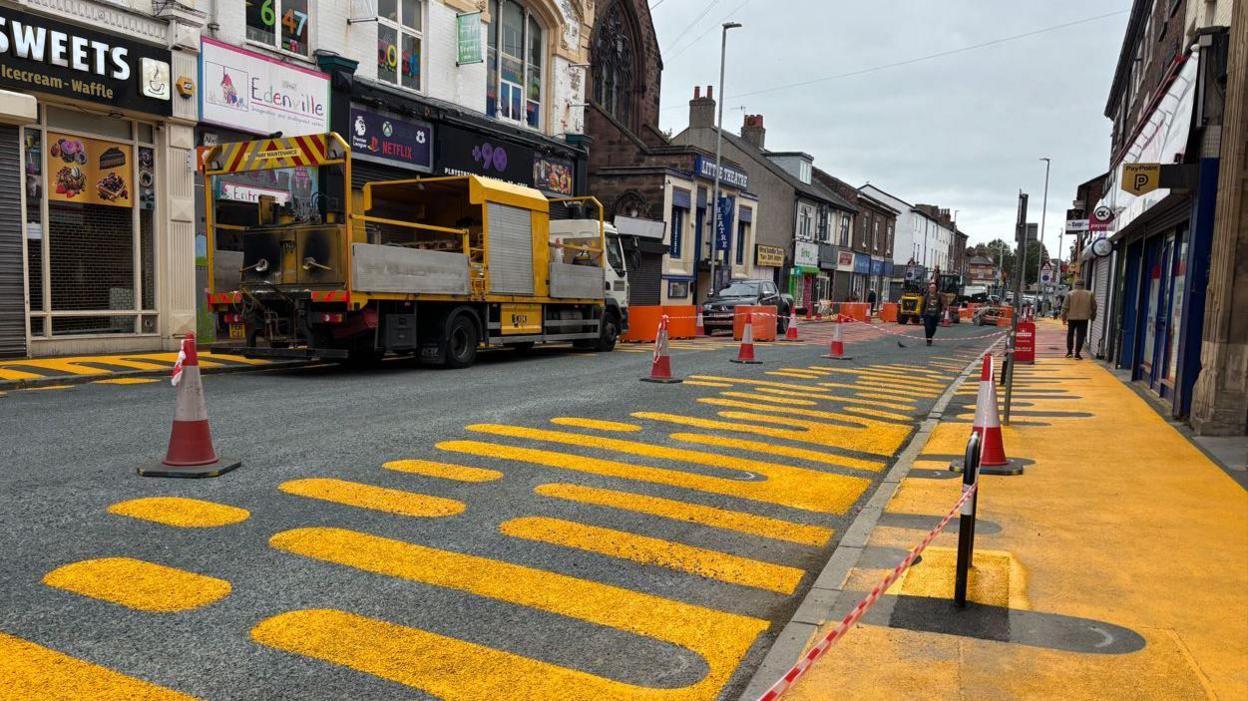 Cones run along a freshly painted street, with yellow markings in an unusual pattern set along the pavement. 