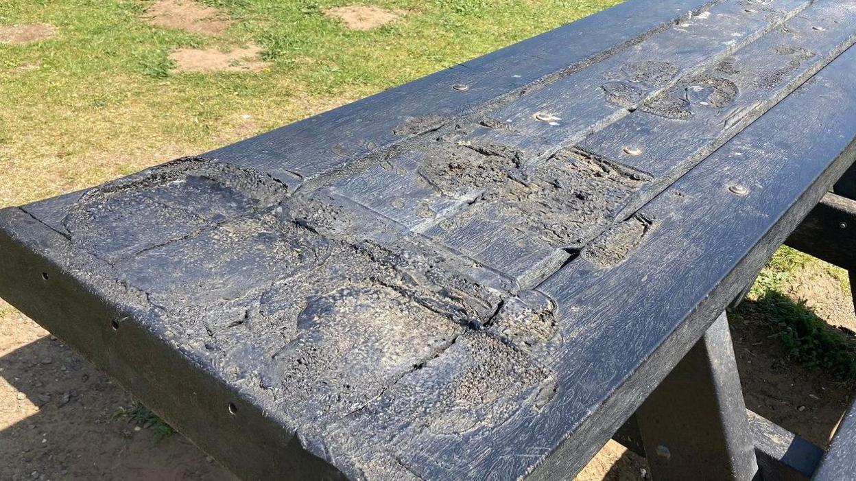A black picnic bench with several large melted patches on top