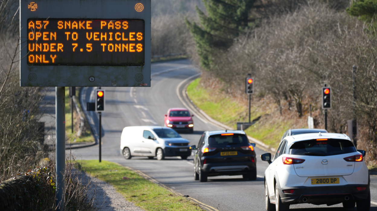 Road with cars on and greenary on either side, with electronic sign saying "A57 Snake Pass open to vehicles under 7.5 tonnes only"