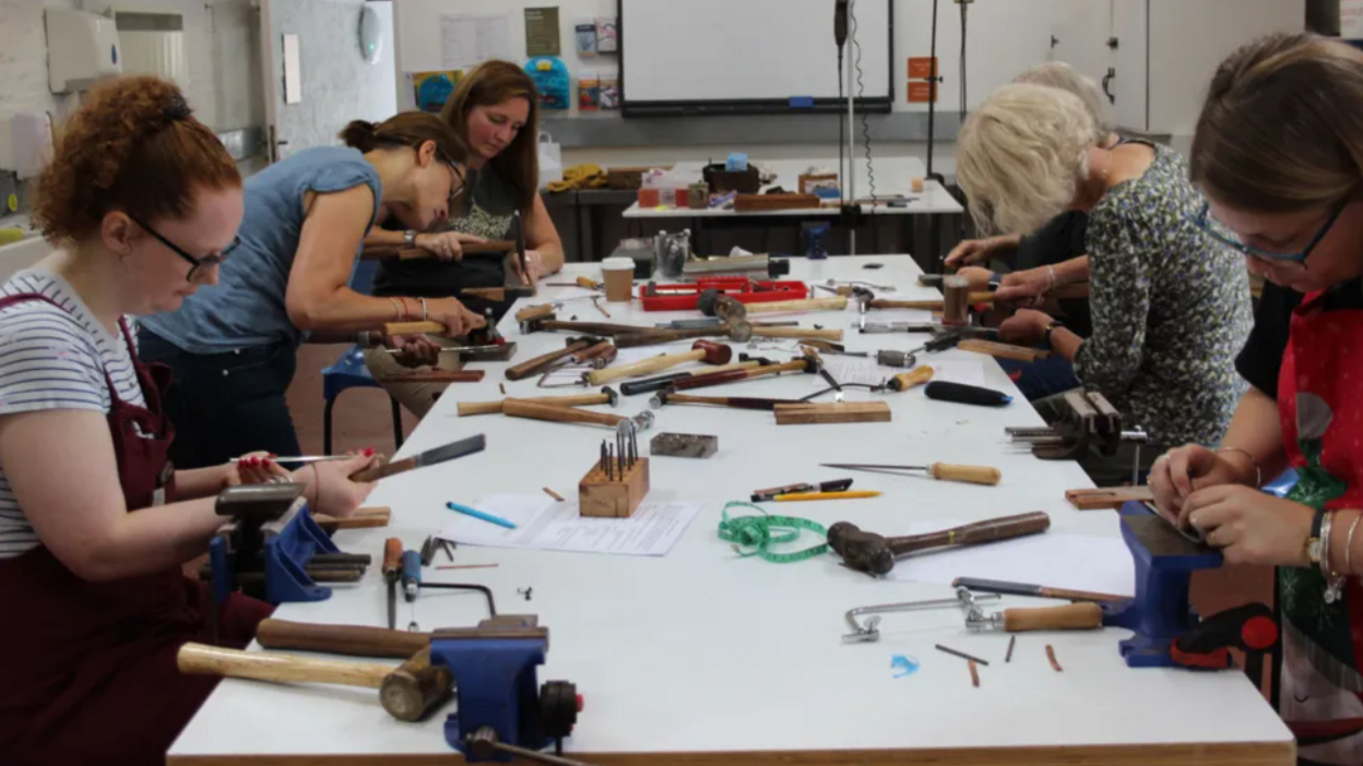 Six women working at a table of hammers and vices