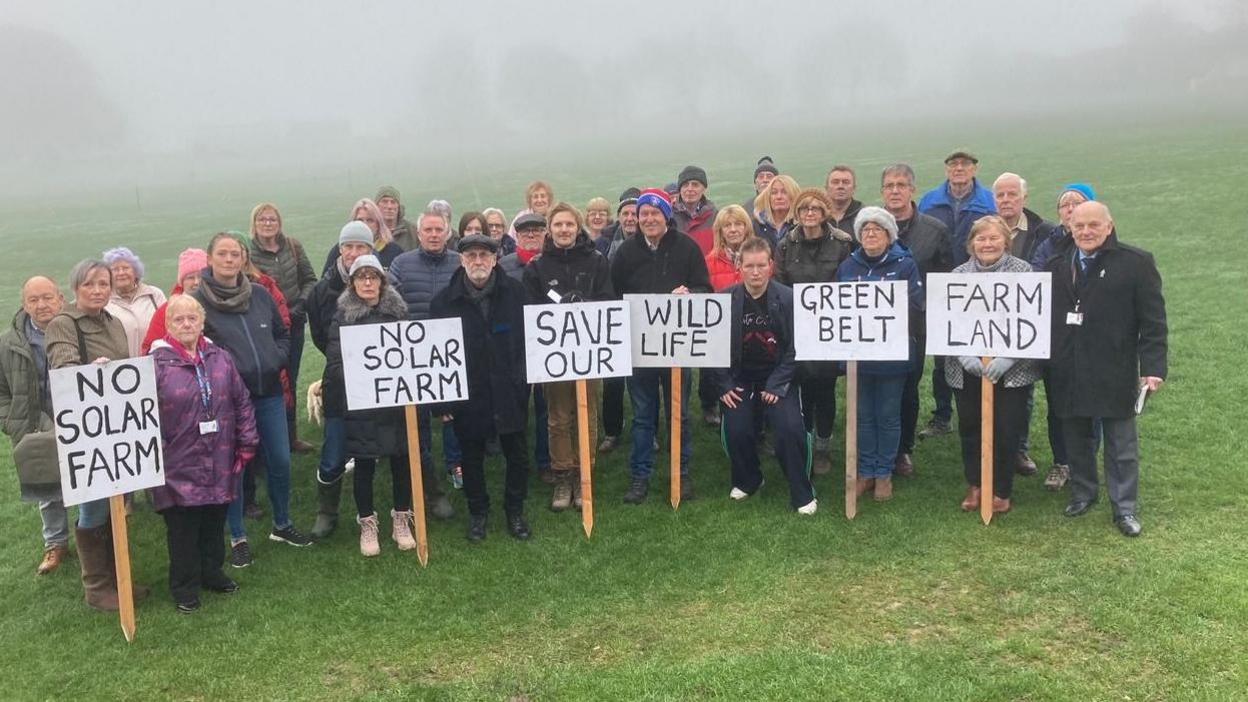 Group of men and women carrying signs reading Save our Wildlife and No Solar Farm 