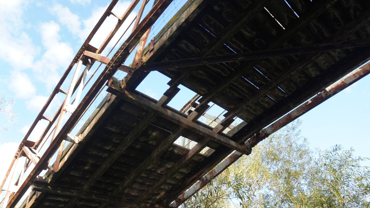 A view of the Works bridge at Attenborough Nature Reserve from underneath it, showing a hole in the bridge and rusting of the structure.