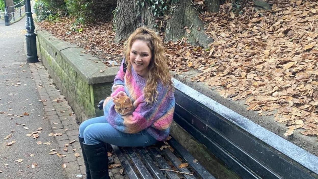 Raymond the ginger tom cat sitting on the lap of a smiling woman in the park