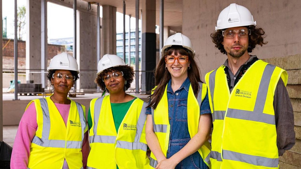 A group of people stand inside a derelict building. They are wearing hard hats and high-vis jackets