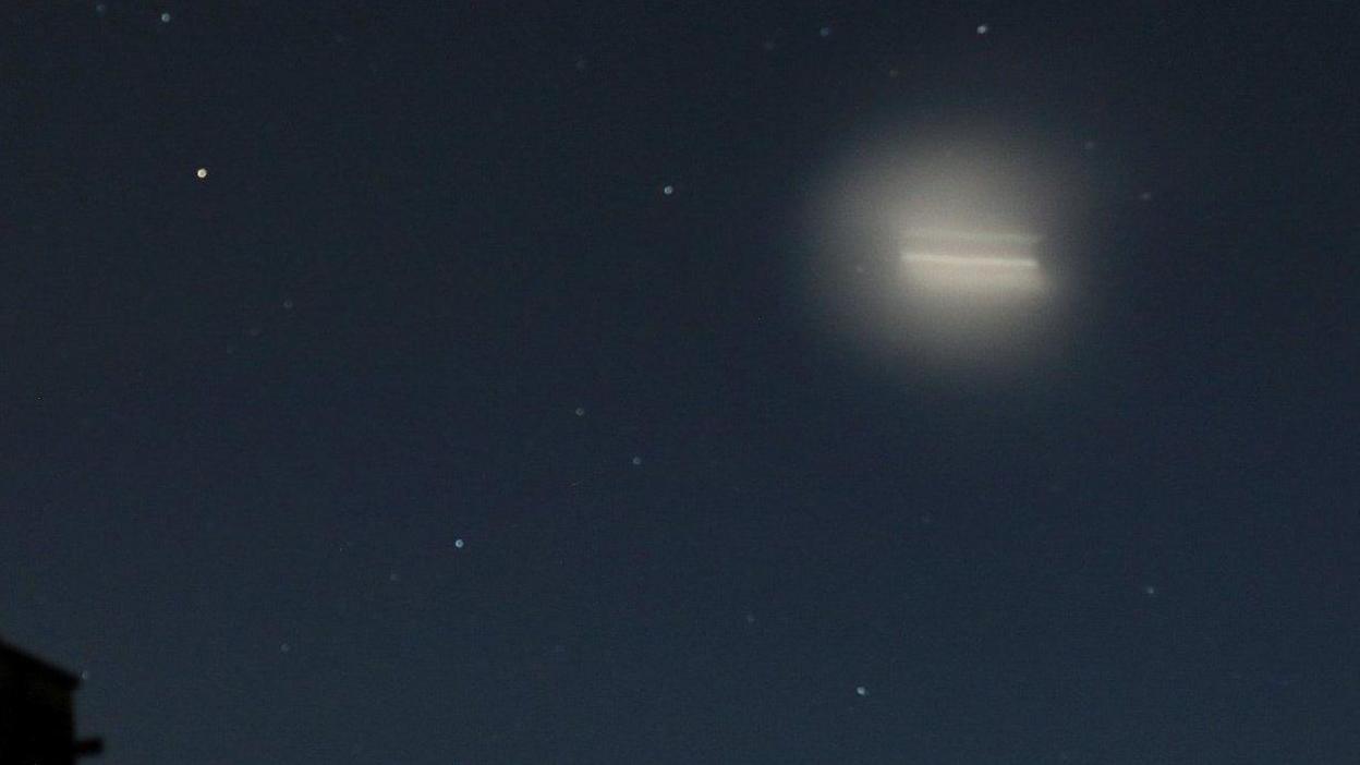 A dark blue sky with a bright light travelling across the sky. 