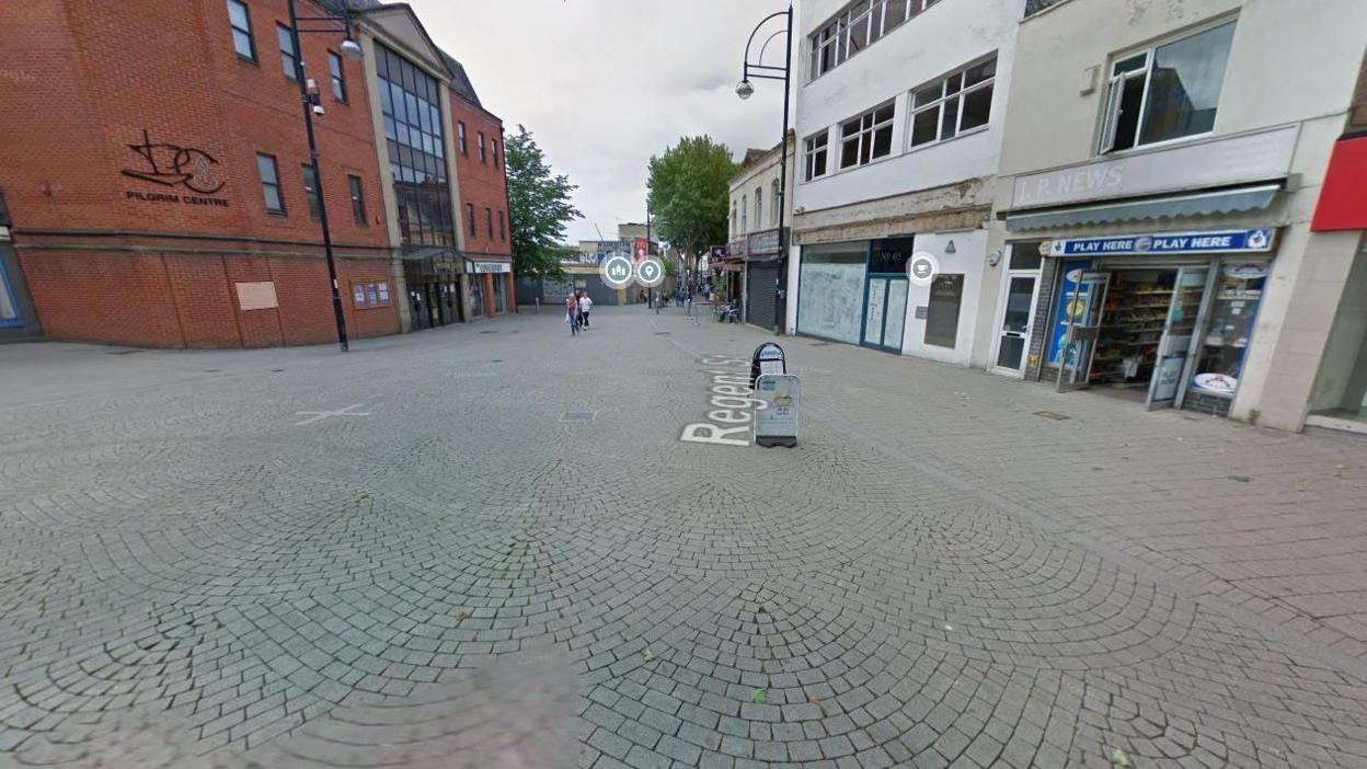 A high street in Swindon with several shops. Some people can be seen walking in the distance.