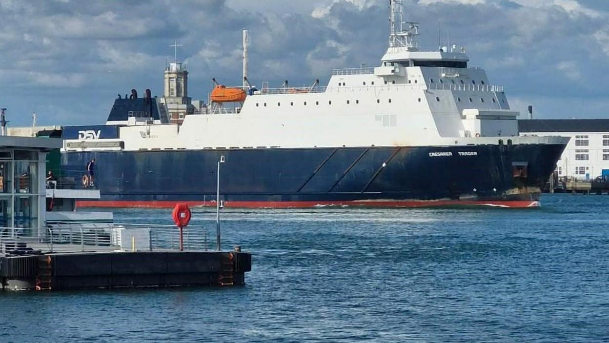A cargo ship anchored at sea with visible smoke rising from its deck during a firefighting response off the Isle of Wight coastline.