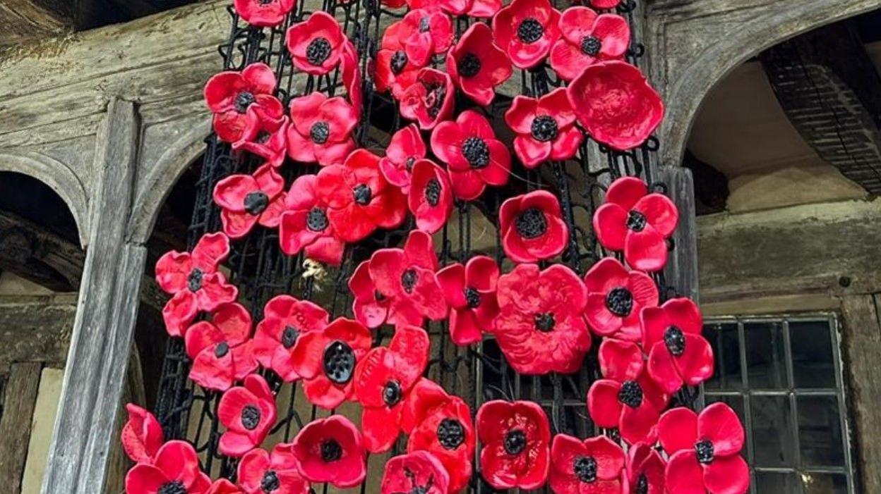 Dozens of ceramic poppies in a half-timbered medieval courtyard.