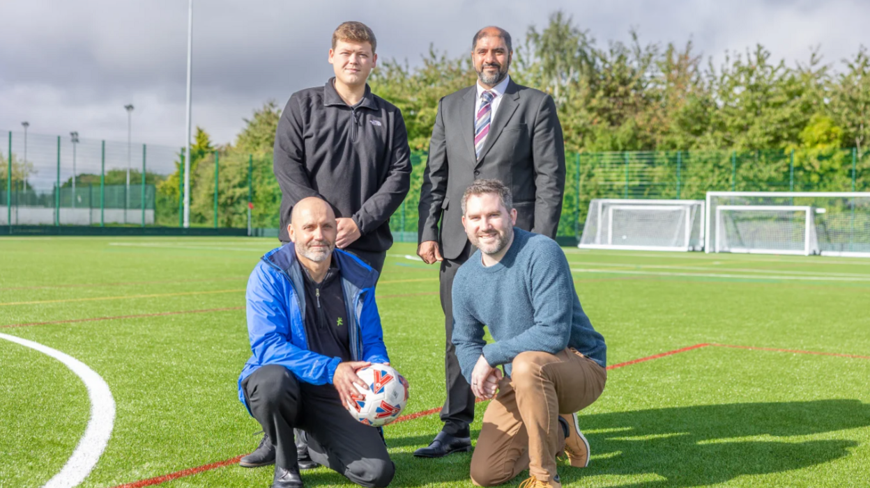 Jack Handsaker, Jabba Riaz, Alan New and Martin Collier standing on the new all weather pitch, with one of the men holding a football