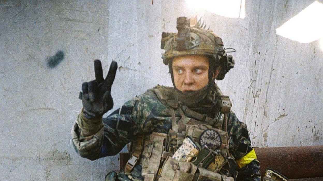 A unformed Ukrainian soldier does the peace sign to the camera