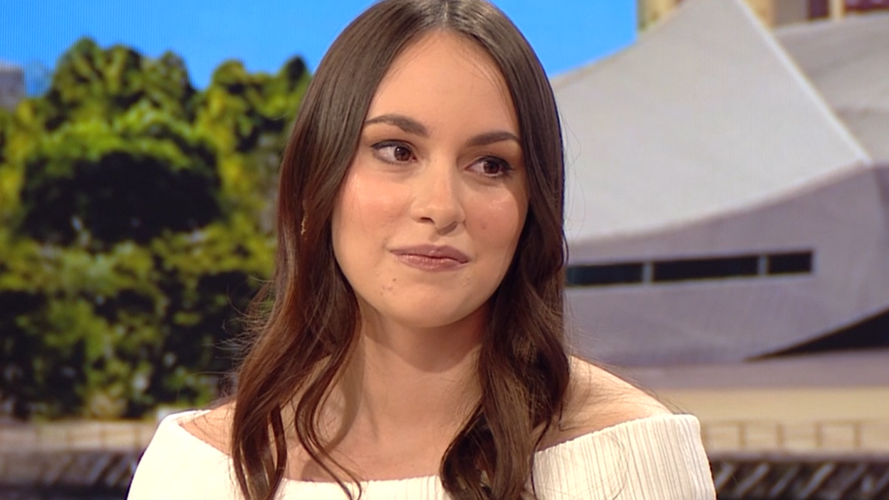 A woman with long brown hair and a white top sat in a TV studio