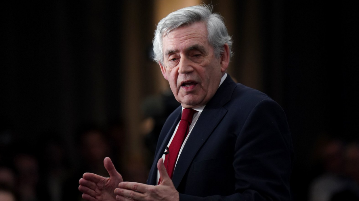 Gordon Brown addresses an audience wearing a navy suit, a white shirt and a red tie 