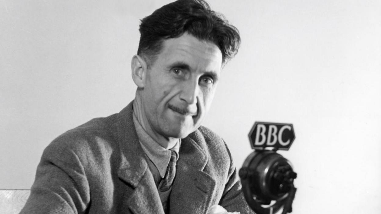 George Orwell smiling for the camera in front of a BBC microphone.