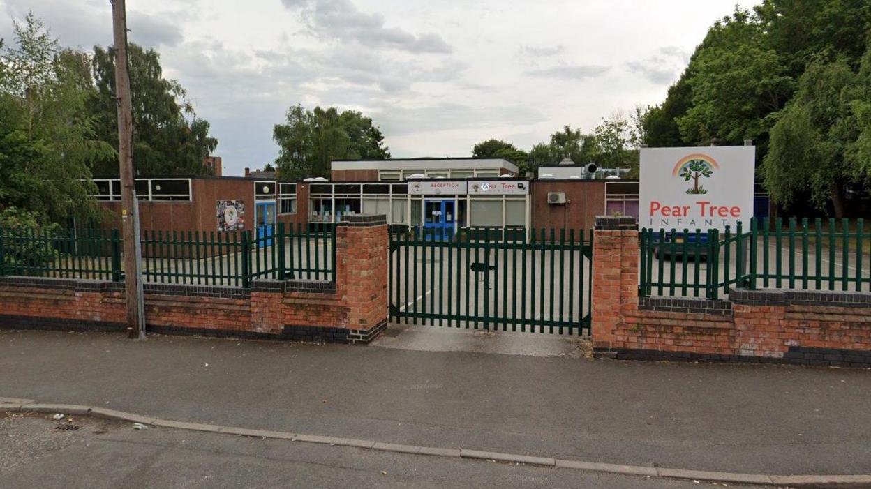 The single-storey school is seen behind green school gates.