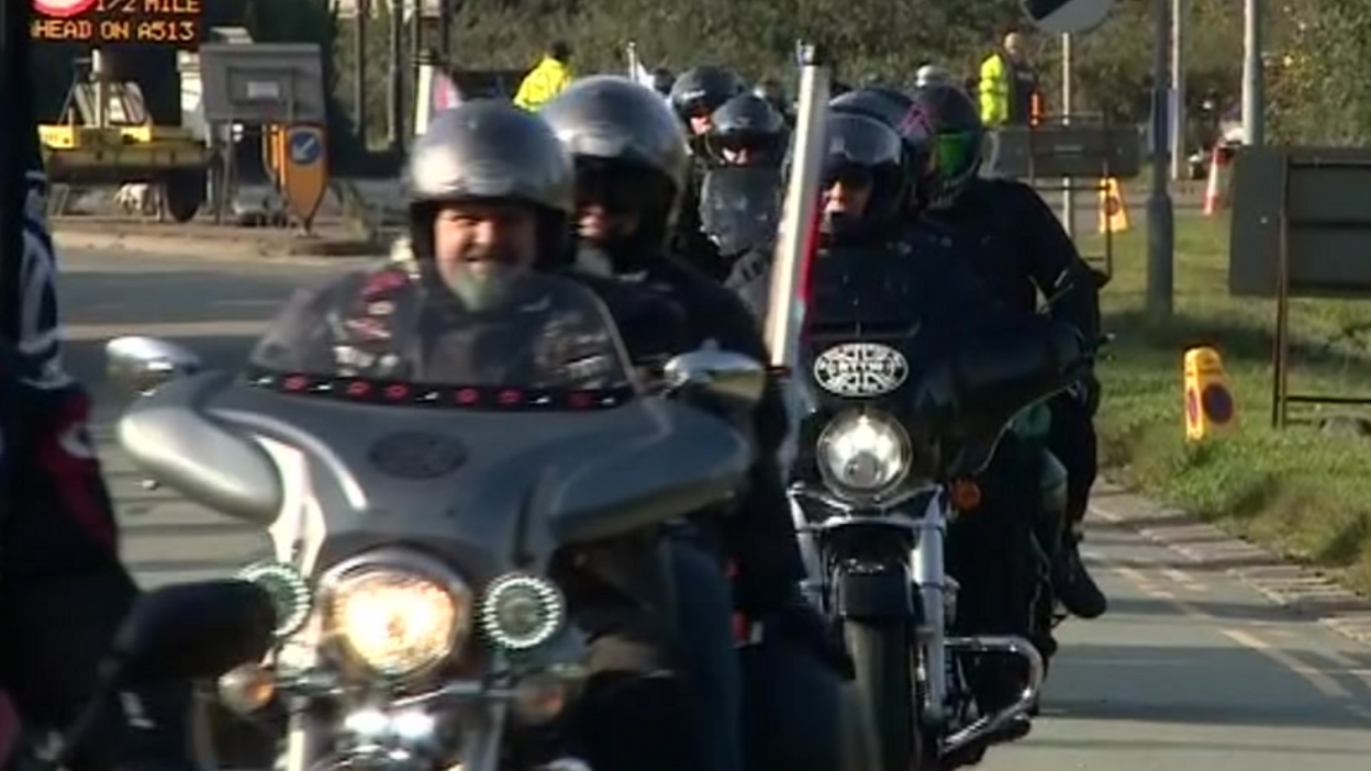 A row of motorcycles approach the camera, the rider at the front smiling