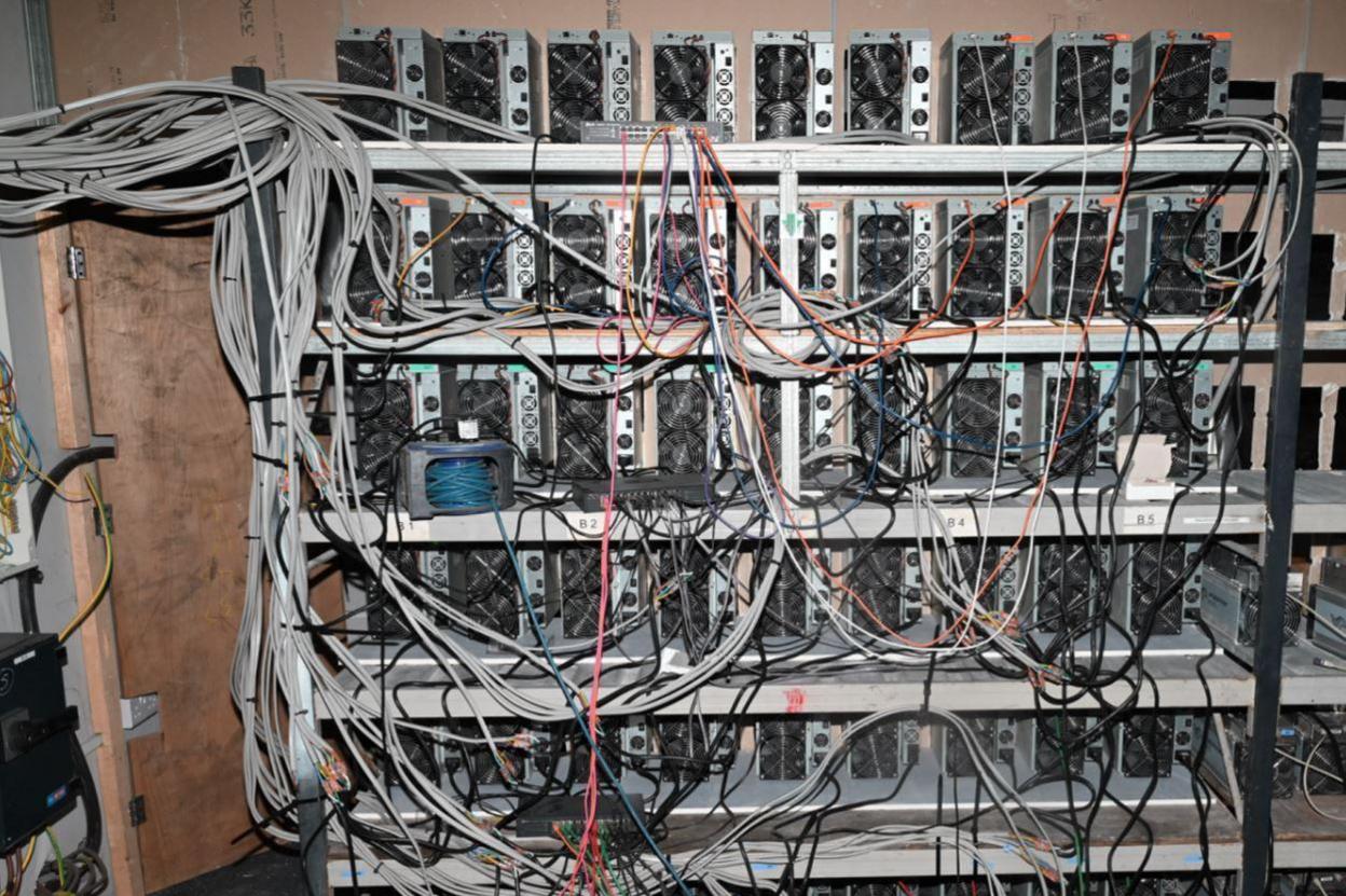 A series of machines being used to mine cryptocurrency. A series of wires are protruding from the machines.
