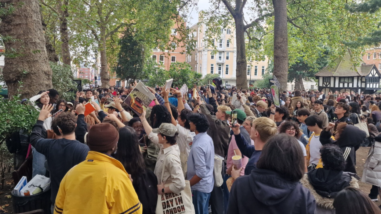 More than a hundred people gathered in Soho Square. A group of men crowd around an event organiser and hold up books and vinyl records they have brought with them.  